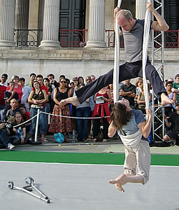 Claire is swinging in front of the National Gallery, her back supported by a hanging sheet. Jami is above her, holding onto the sheet with his two arms. Claire's crutches are lying on the floor beneath.