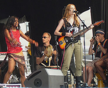 A girl plays electric guitar while another girl dances and a man plays the tambourine