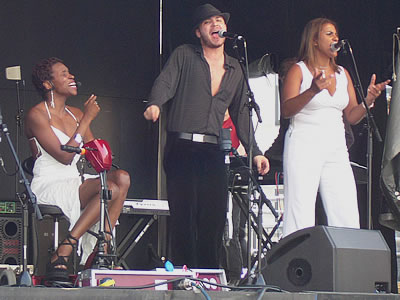 Minika Green, on the left,  is singing wonderfully from her scooter-style wheelchair. She is accompanied by a male and female singer. The ladies are all dressed in white, and the man in black